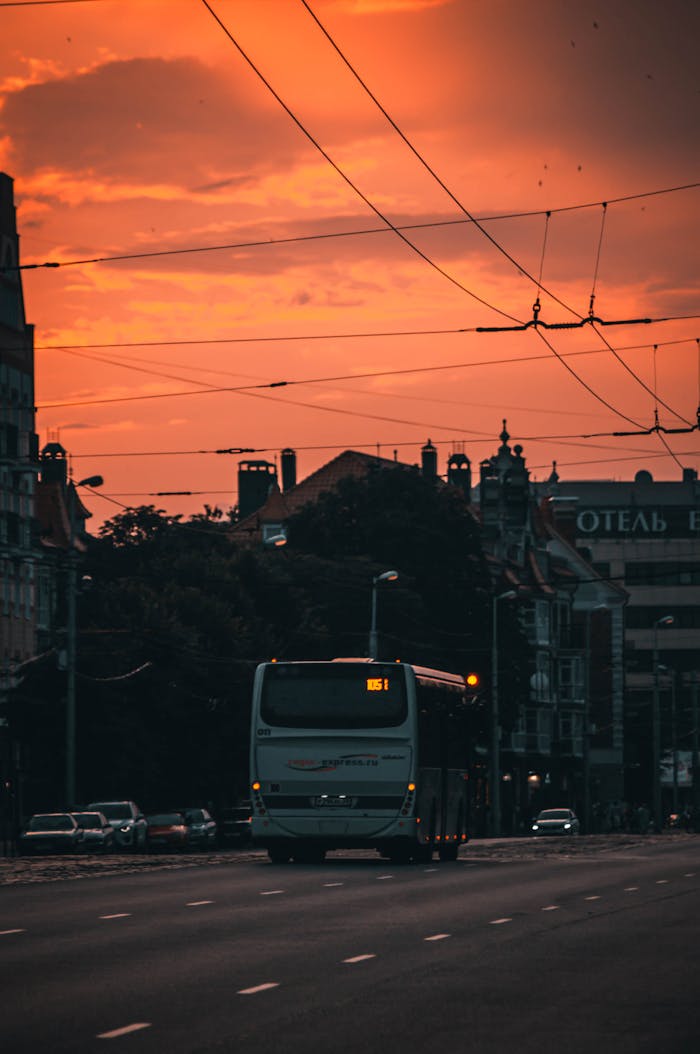 A bus travels down a city road at dusk in Kaliningrad, Russia, with vibrant orange sky.